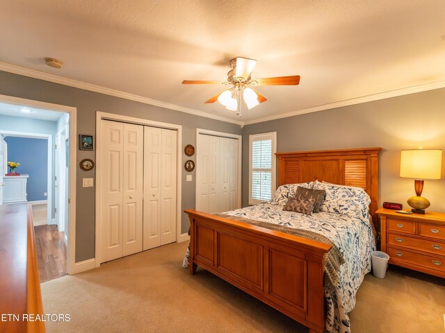 carpeted bedroom with crown molding, ceiling fan, and multiple closets