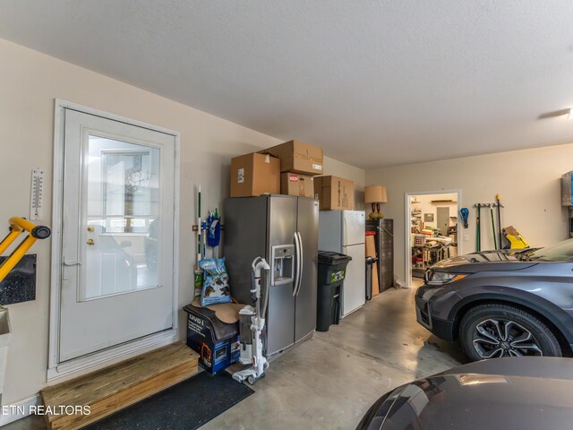 garage with stainless steel refrigerator with ice dispenser and white fridge