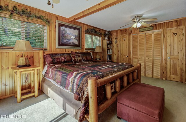 carpeted bedroom featuring a closet, wooden walls, multiple windows, and ceiling fan