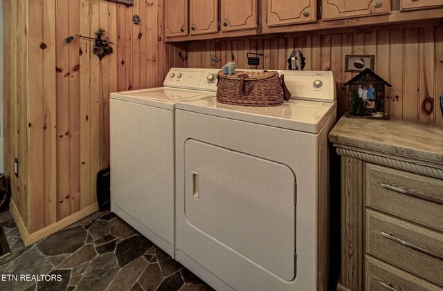 laundry room featuring wood walls, washing machine and clothes dryer, and cabinets