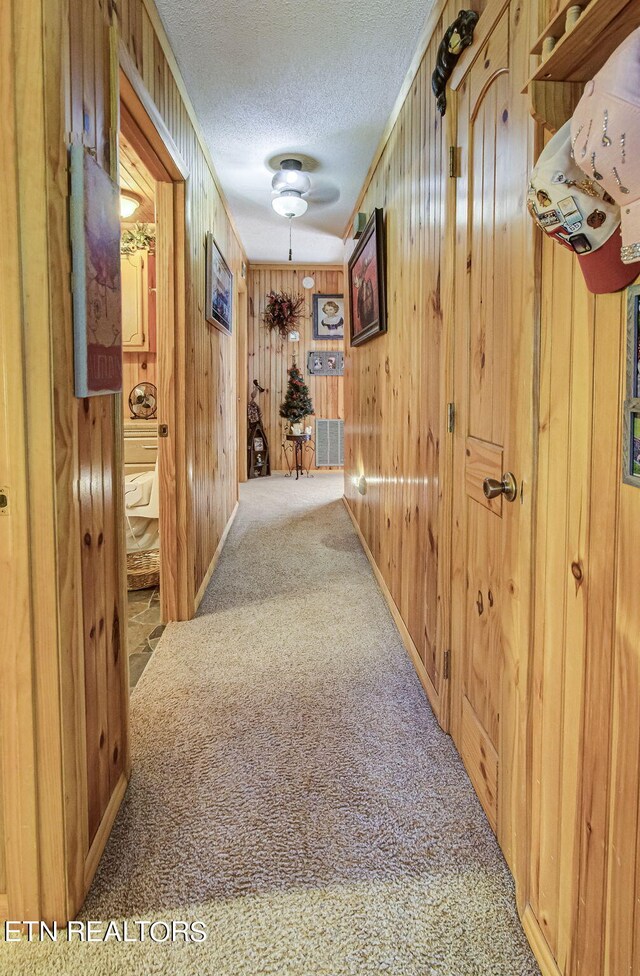 hallway featuring carpet, a textured ceiling, and wood walls