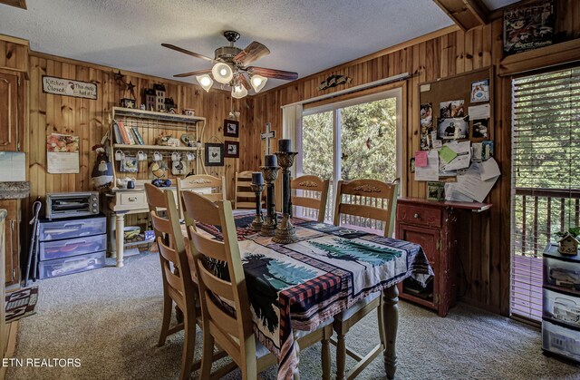 carpeted dining room with wood walls, ceiling fan, and a textured ceiling