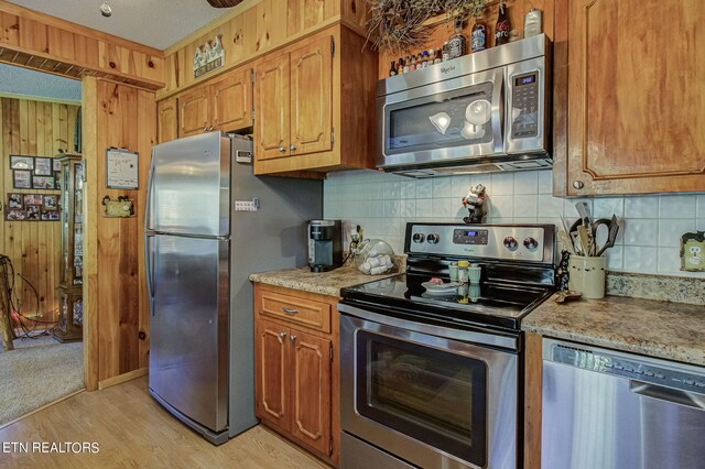 kitchen featuring appliances with stainless steel finishes, light wood-type flooring, wood walls, and decorative backsplash