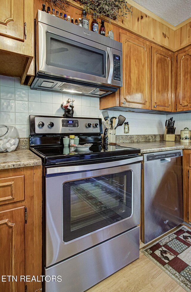 kitchen featuring a textured ceiling, appliances with stainless steel finishes, light hardwood / wood-style floors, and decorative backsplash