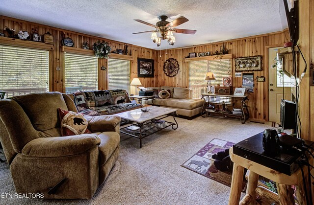 carpeted living room with a textured ceiling, wood walls, ceiling fan, and plenty of natural light