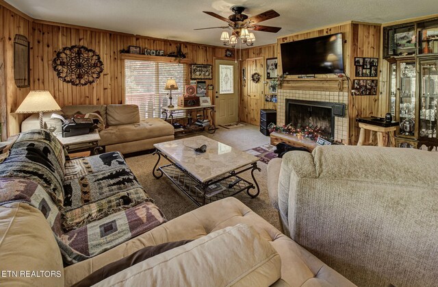 carpeted living room with wooden walls, ceiling fan, a fireplace, and a textured ceiling