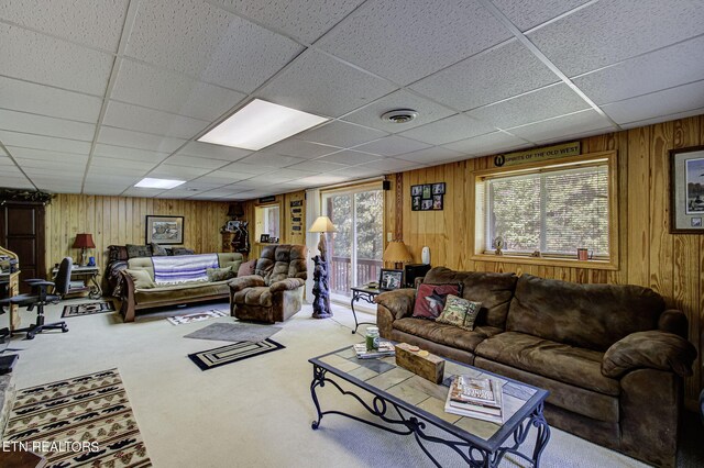 carpeted living room with a paneled ceiling and wood walls