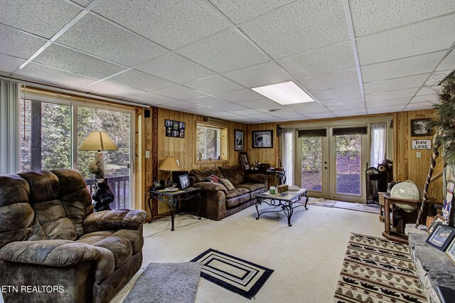 carpeted living room with wooden walls, french doors, and a paneled ceiling