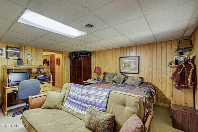 carpeted bedroom featuring a paneled ceiling and wood walls