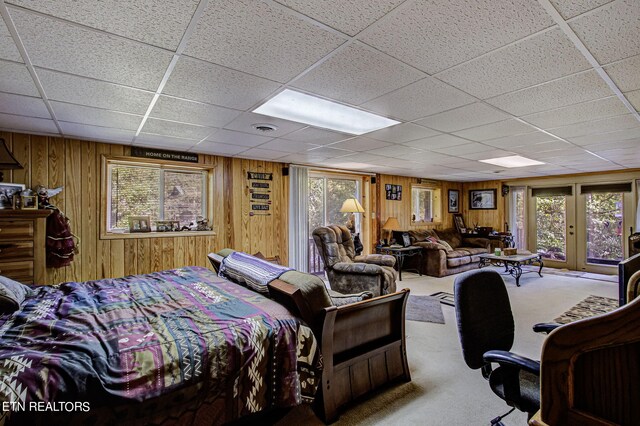 carpeted bedroom with french doors, a drop ceiling, wood walls, and multiple windows