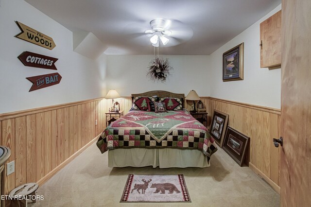 bedroom featuring ceiling fan, light carpet, and wood walls