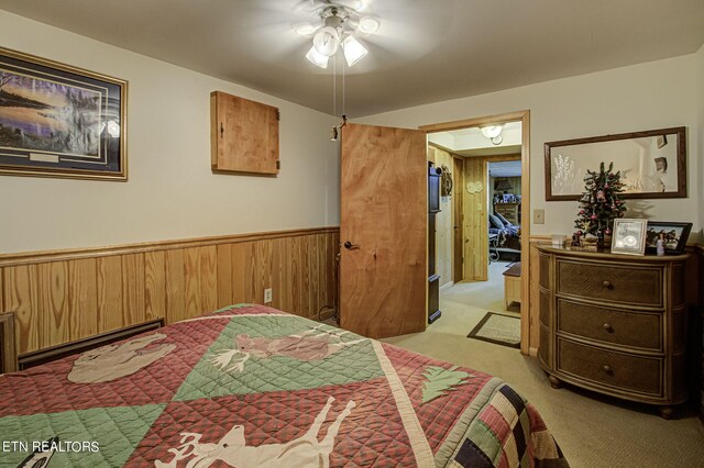 carpeted bedroom featuring ceiling fan, a baseboard radiator, and wooden walls