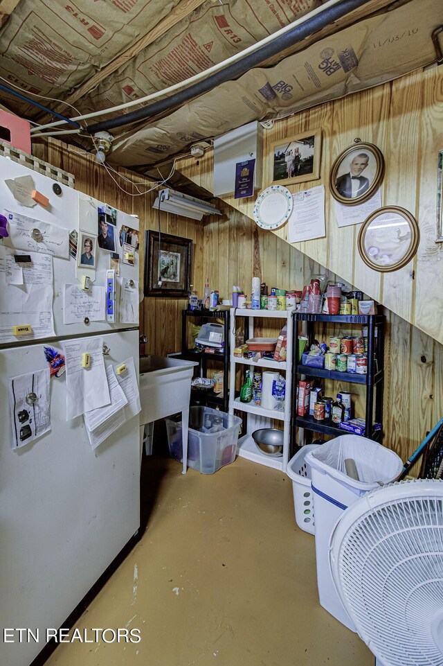 basement with wood walls and white refrigerator