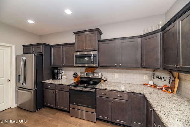 kitchen featuring appliances with stainless steel finishes, light stone counters, tasteful backsplash, light wood-type flooring, and dark brown cabinetry