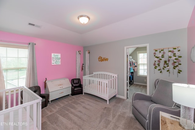 carpeted bedroom featuring multiple windows, a crib, a walk in closet, and a closet