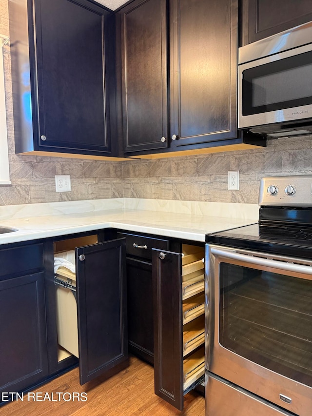 kitchen with light stone counters, decorative backsplash, stainless steel appliances, and light hardwood / wood-style flooring