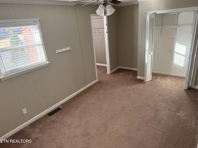 unfurnished bedroom featuring ceiling fan, light colored carpet, a closet, and wood walls