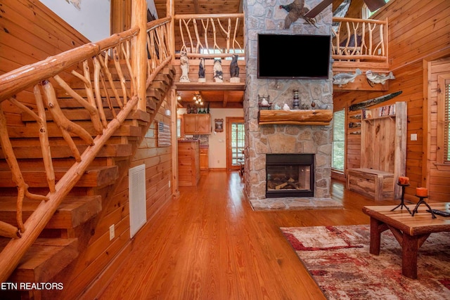 unfurnished living room featuring a high ceiling, a stone fireplace, wood walls, and hardwood / wood-style floors