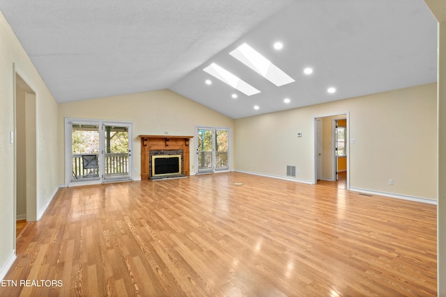 unfurnished living room featuring vaulted ceiling with skylight, light hardwood / wood-style floors, and a healthy amount of sunlight