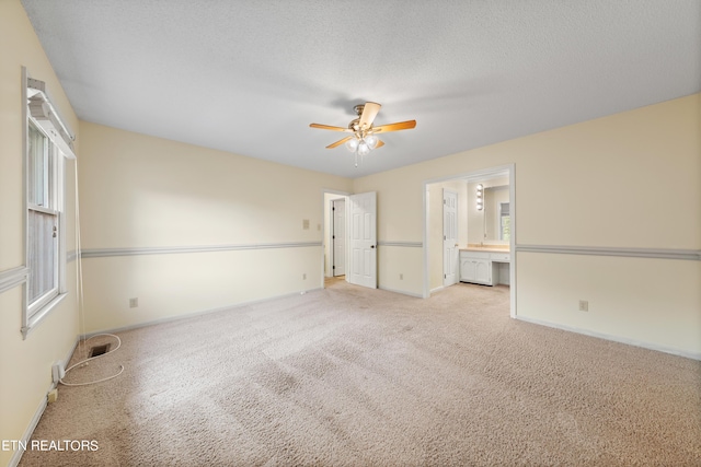 unfurnished bedroom with a textured ceiling, connected bathroom, light carpet, and ceiling fan