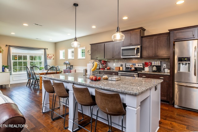 kitchen with pendant lighting, a center island with sink, stainless steel appliances, and dark hardwood / wood-style flooring