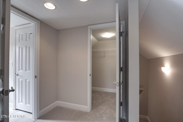 hall with lofted ceiling, light colored carpet, a textured ceiling, and baseboards