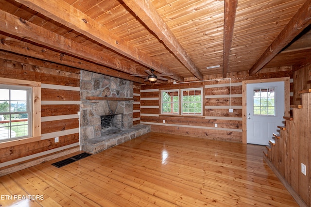 unfurnished living room with wood ceiling, beam ceiling, light hardwood / wood-style flooring, wooden walls, and a stone fireplace