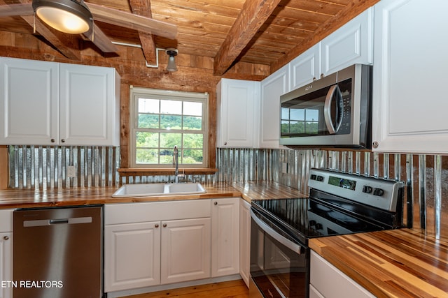 kitchen with stainless steel appliances, white cabinetry, butcher block counters, and beamed ceiling