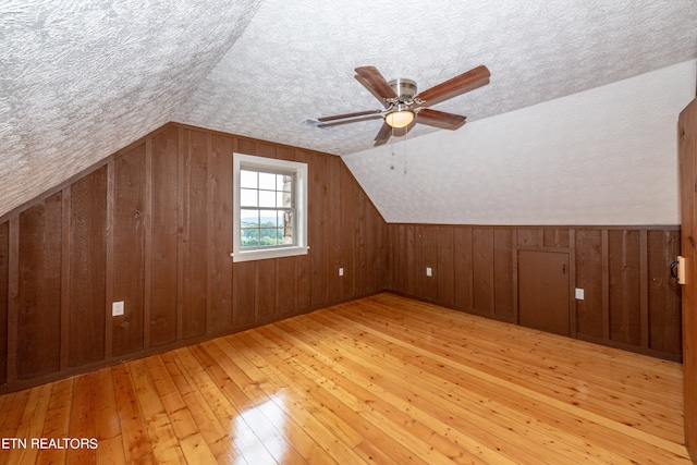 additional living space featuring light wood-type flooring, lofted ceiling, a textured ceiling, and wooden walls