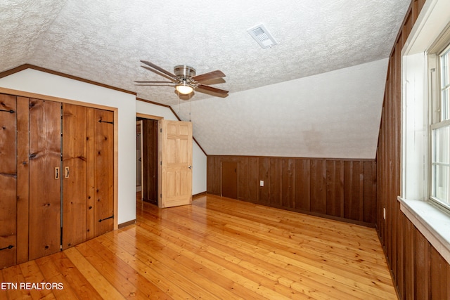 bonus room with a textured ceiling, lofted ceiling, wood walls, light hardwood / wood-style flooring, and ceiling fan