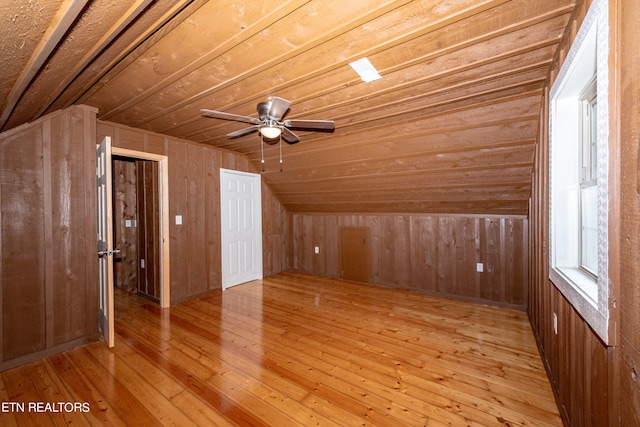 additional living space featuring lofted ceiling, wooden walls, ceiling fan, and light hardwood / wood-style flooring