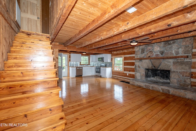 unfurnished living room featuring light hardwood / wood-style floors, beamed ceiling, wooden ceiling, and a stone fireplace