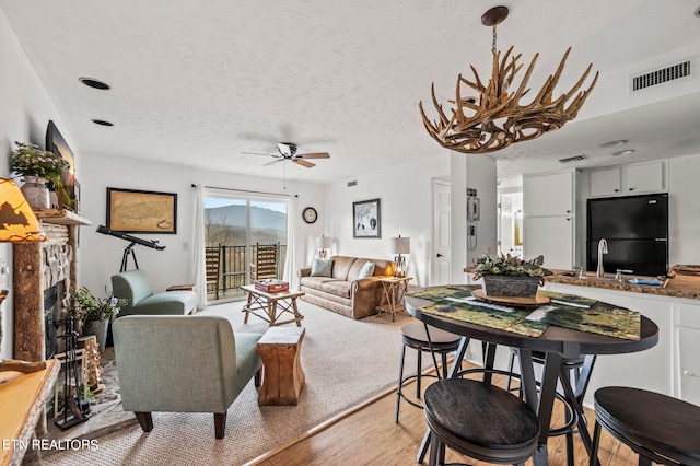 dining space featuring light wood-type flooring, a textured ceiling, sink, and ceiling fan