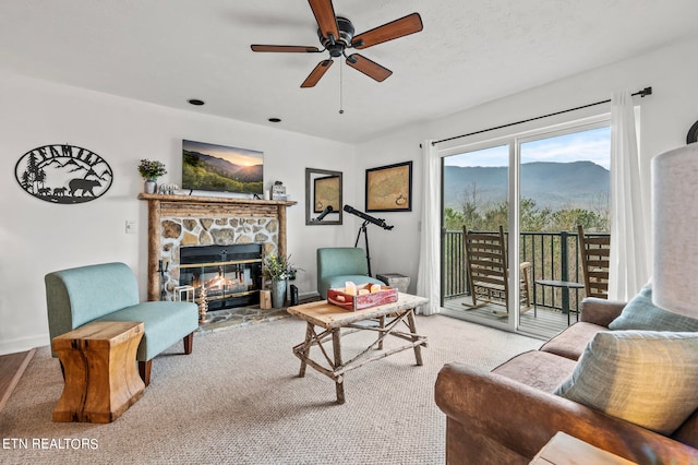 living room featuring ceiling fan, a mountain view, carpet floors, and a stone fireplace