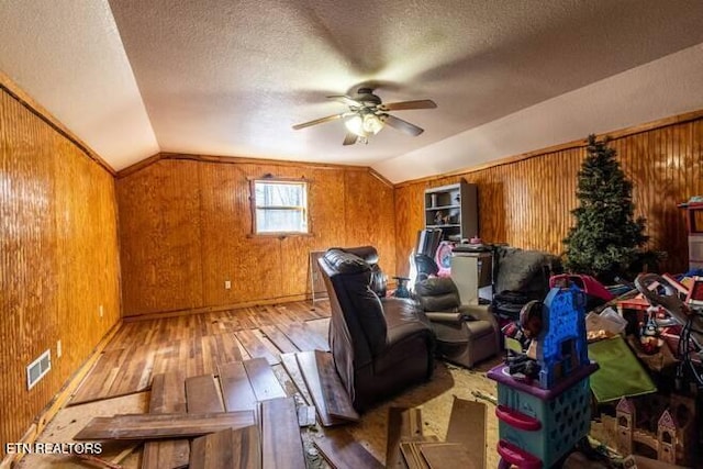 additional living space with wood-type flooring, wooden walls, vaulted ceiling, and ceiling fan