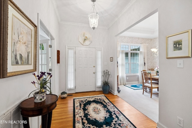 foyer entrance featuring light wood-type flooring, crown molding, and a chandelier