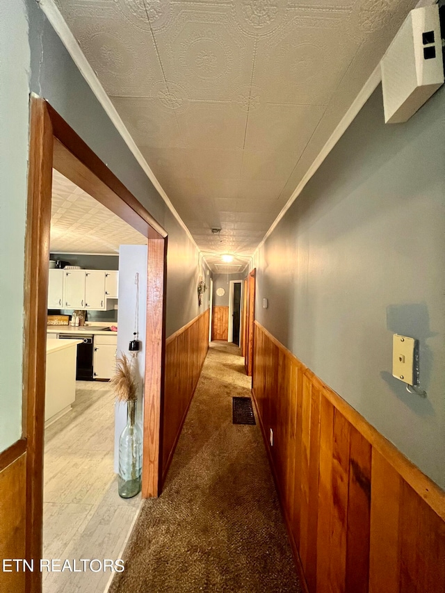 hallway with a textured ceiling, ornamental molding, wooden walls, and light carpet