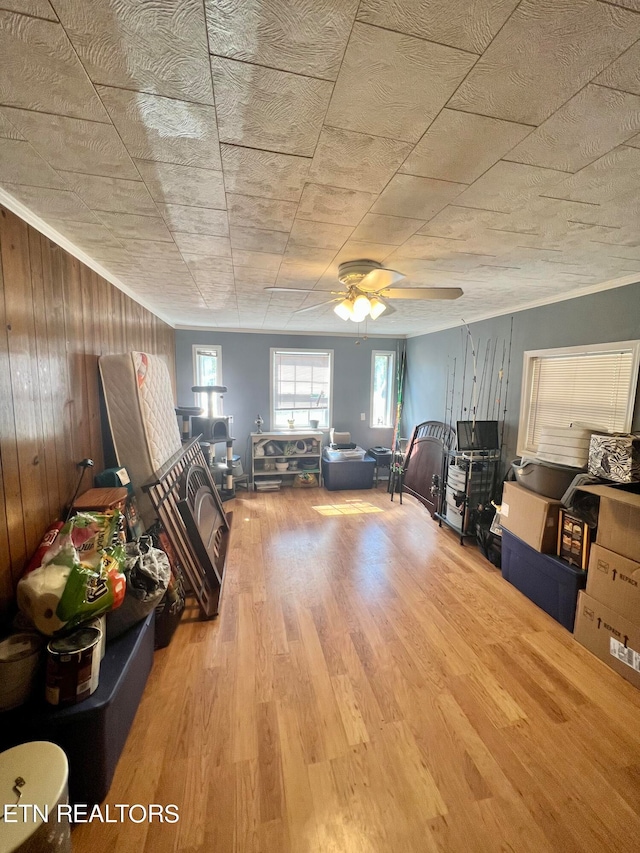 unfurnished living room featuring wood-type flooring, wood walls, ceiling fan, and crown molding