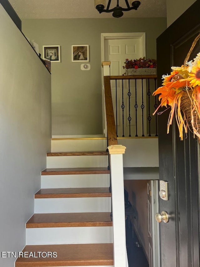 staircase with a notable chandelier and a textured ceiling