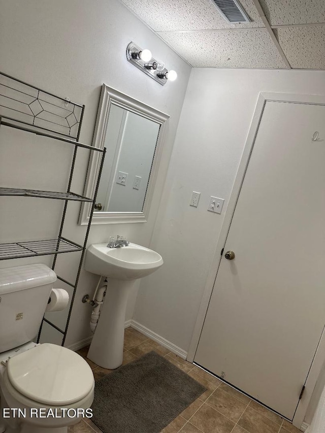 bathroom with a drop ceiling, tile patterned floors, and toilet