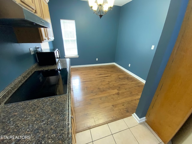 kitchen featuring black cooktop, dark stone counters, a notable chandelier, and light wood-type flooring