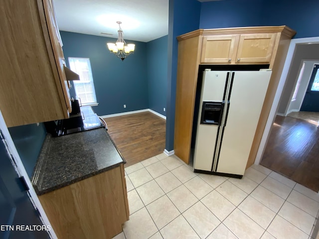 kitchen featuring pendant lighting, light hardwood / wood-style flooring, a notable chandelier, dark stone countertops, and white fridge with ice dispenser