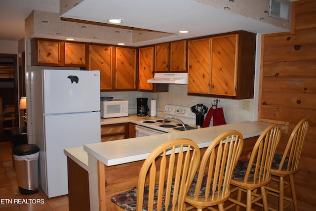 kitchen featuring white appliances, backsplash, kitchen peninsula, and light tile patterned flooring