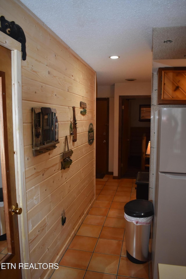 corridor featuring a textured ceiling, wooden walls, and light tile patterned floors