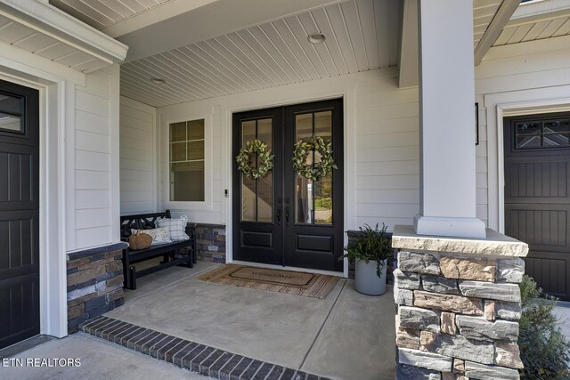doorway to property featuring french doors, stone siding, and covered porch