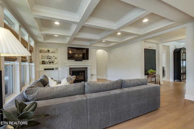 living room with a glass covered fireplace, wood finished floors, beamed ceiling, baseboards, and arched walkways