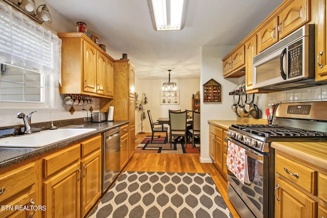 kitchen with hanging light fixtures, sink, appliances with stainless steel finishes, a notable chandelier, and light wood-type flooring