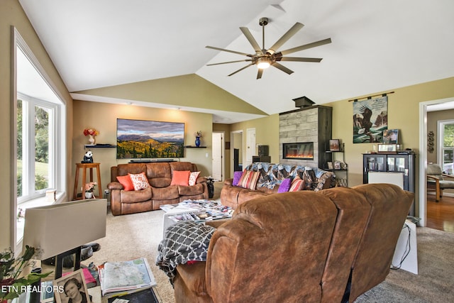 living room with vaulted ceiling, ceiling fan, carpet flooring, and a stone fireplace