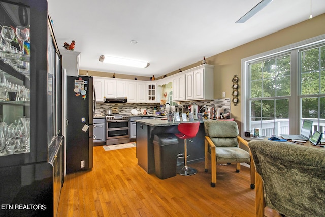 kitchen featuring tasteful backsplash, light wood-type flooring, a peninsula, exhaust hood, and stainless steel appliances