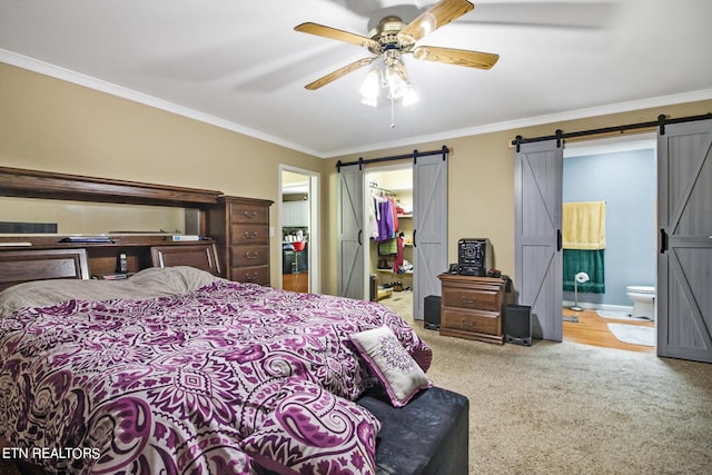 carpeted bedroom featuring a closet, ornamental molding, connected bathroom, a walk in closet, and a barn door
